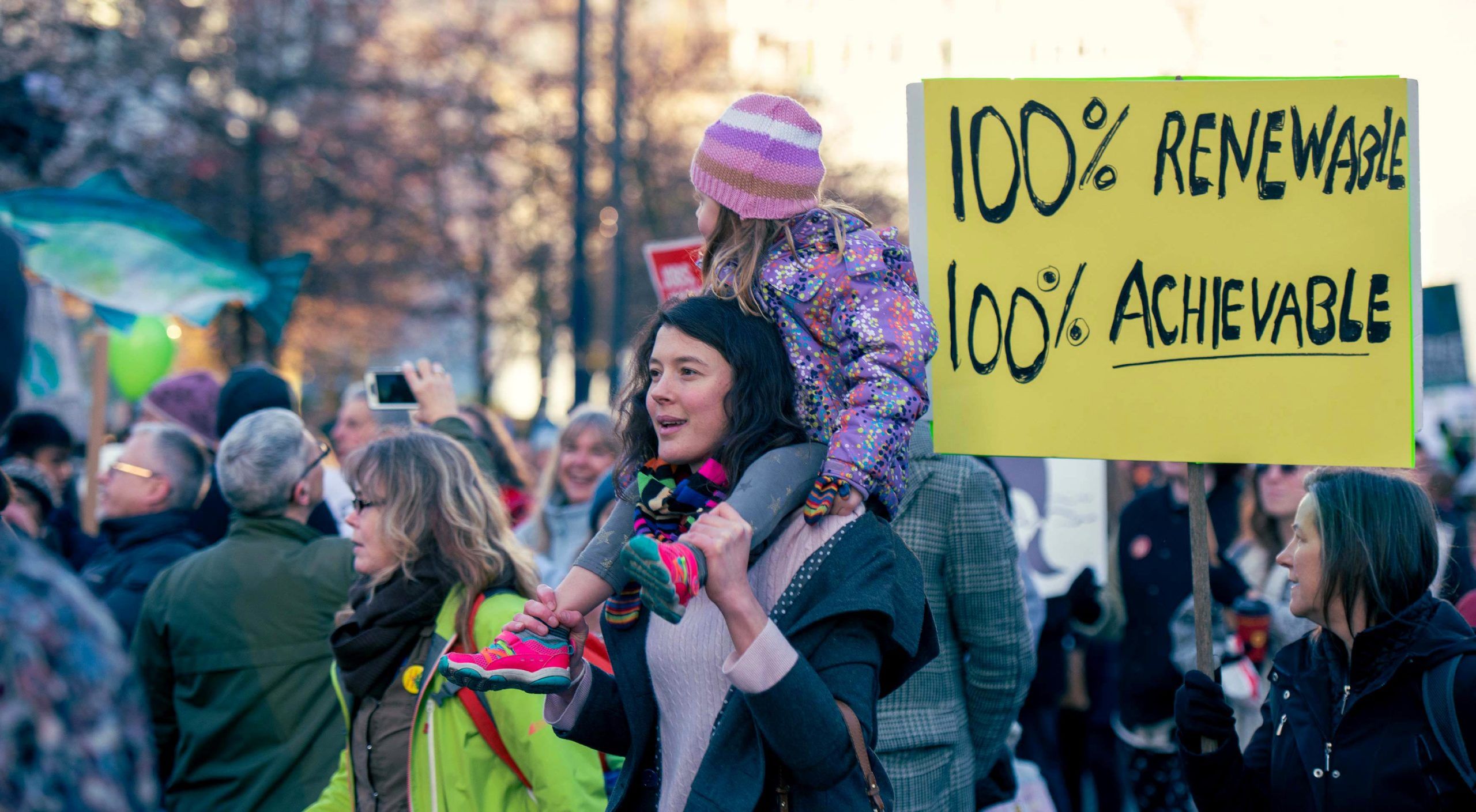 A group of people at a climate change protest. In the centre of the photo is a young woman with a child on her shoulders