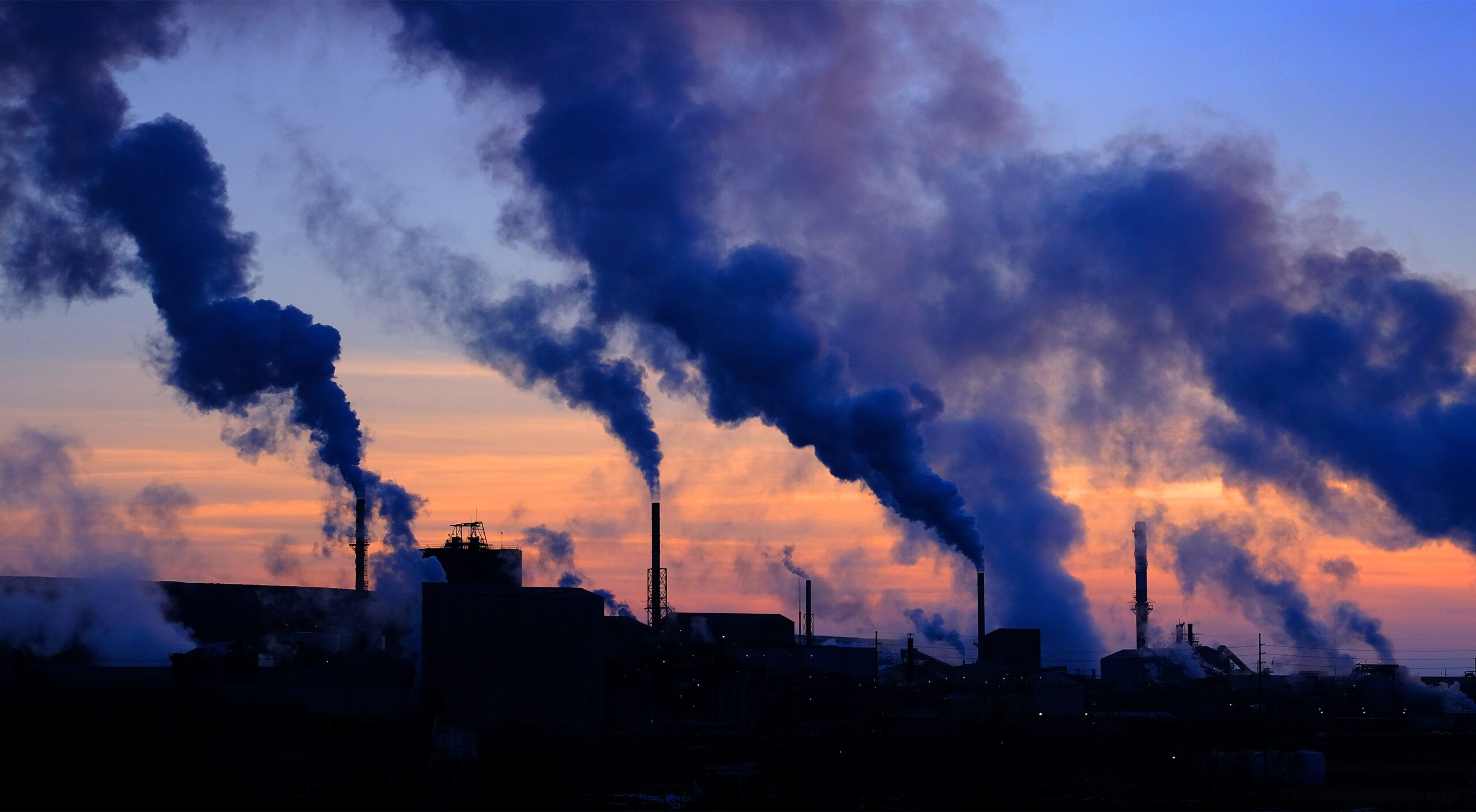 A photo of steam rising from smokestacks in a rural sunset sky.