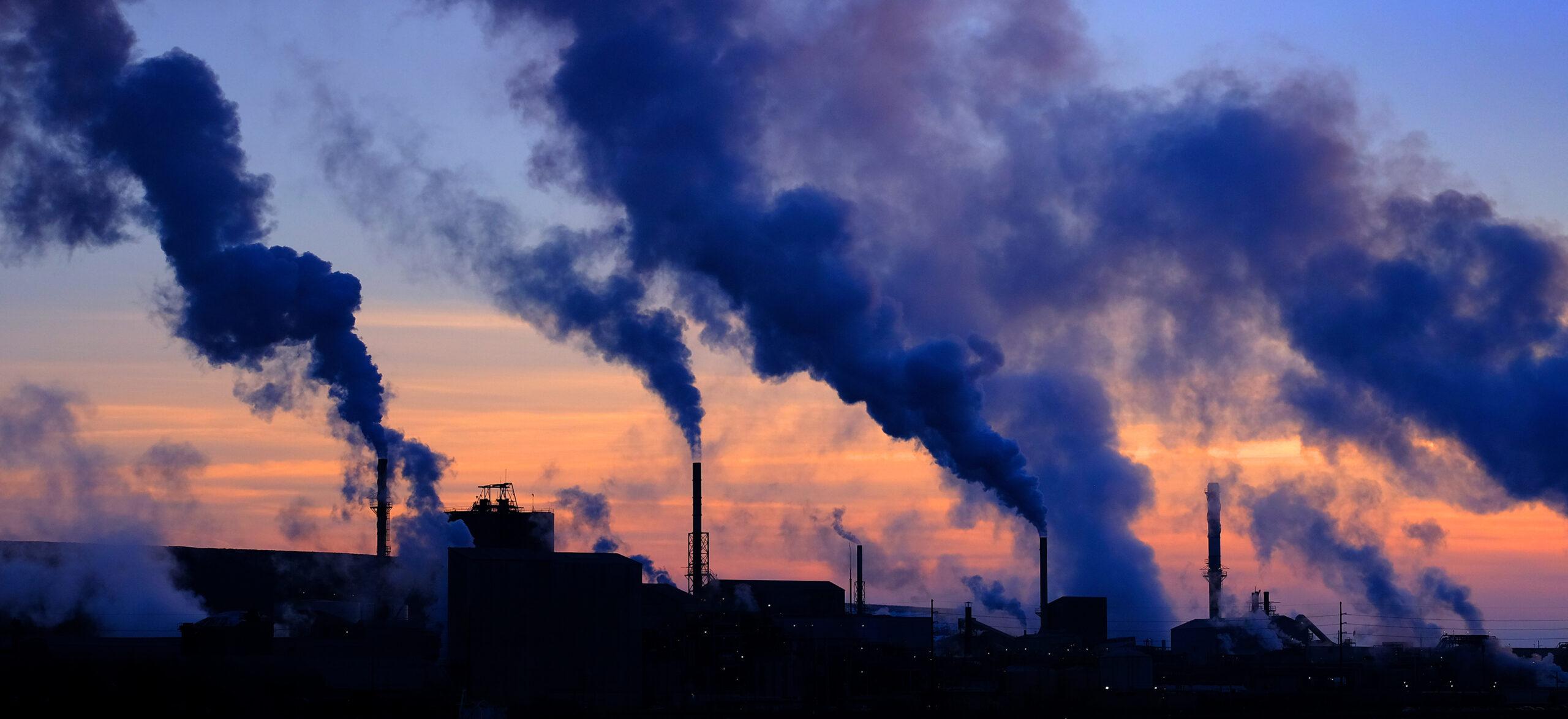 A photo of steam rising from smokestacks in a rural sunset sky.