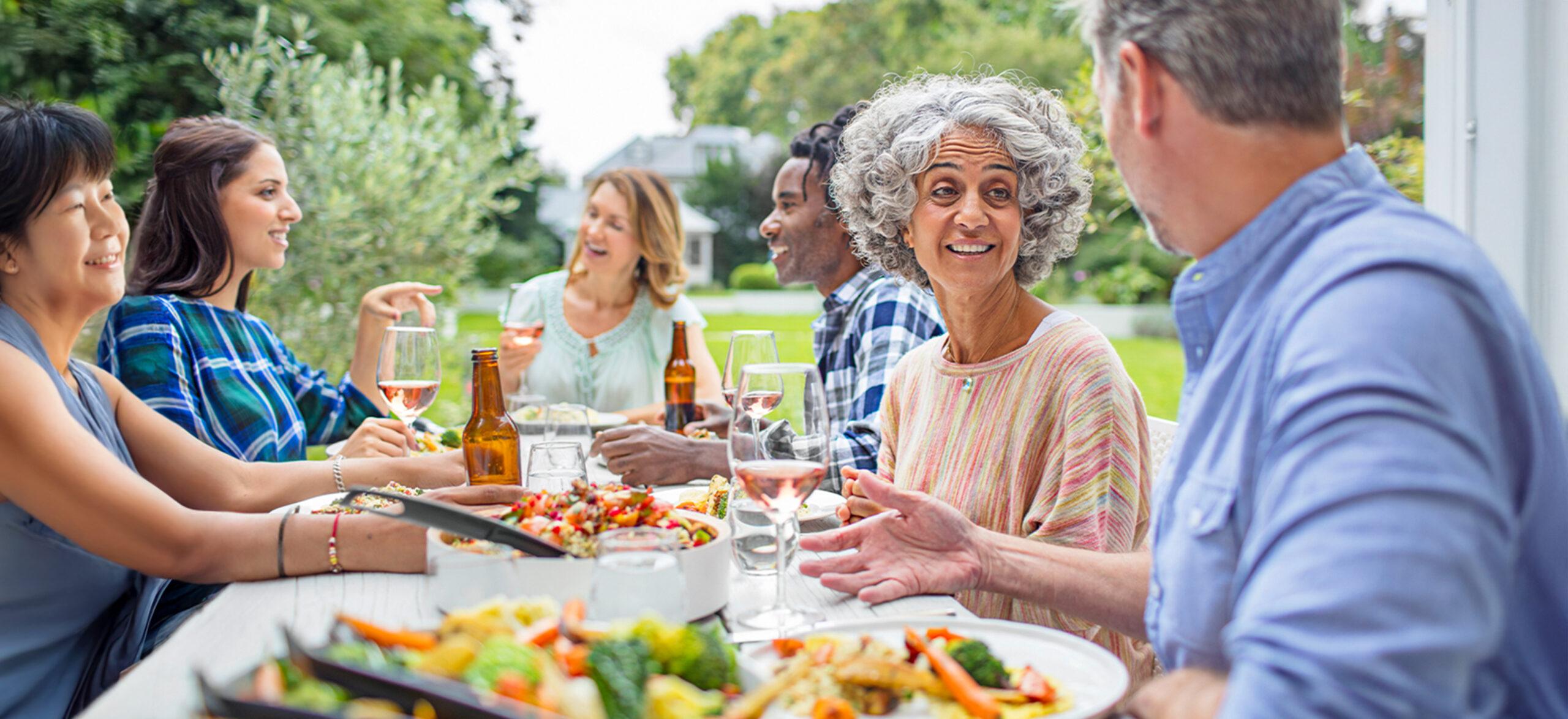 Mature friends talking while having lunch in backyard. Multi-ethnic males and females are enjoying garden party. They are wearing casuals.